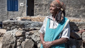 Dame vor ihrem Haus in die Ferne blickend